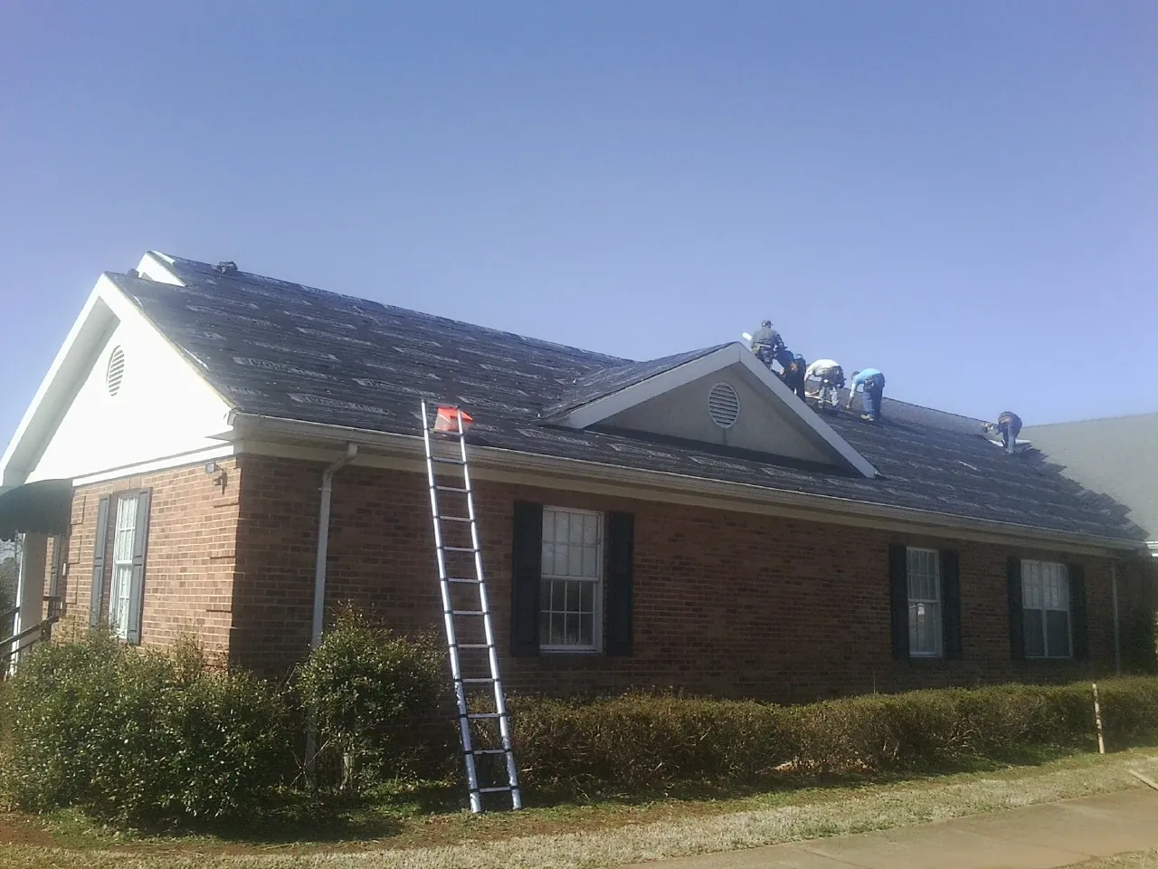 Crew tearing shingles off a brick ranch roof with a ladder set — Metal Roof Repair work by our crew in Hilltown