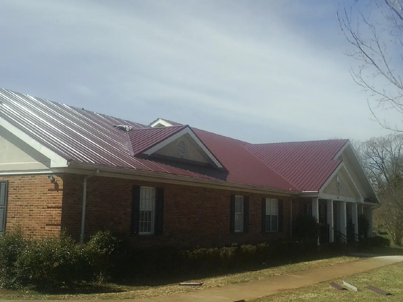 Red metal roof with gabled entries on a long brick building, from a Hail Damage Roof Repair job in Hilltown