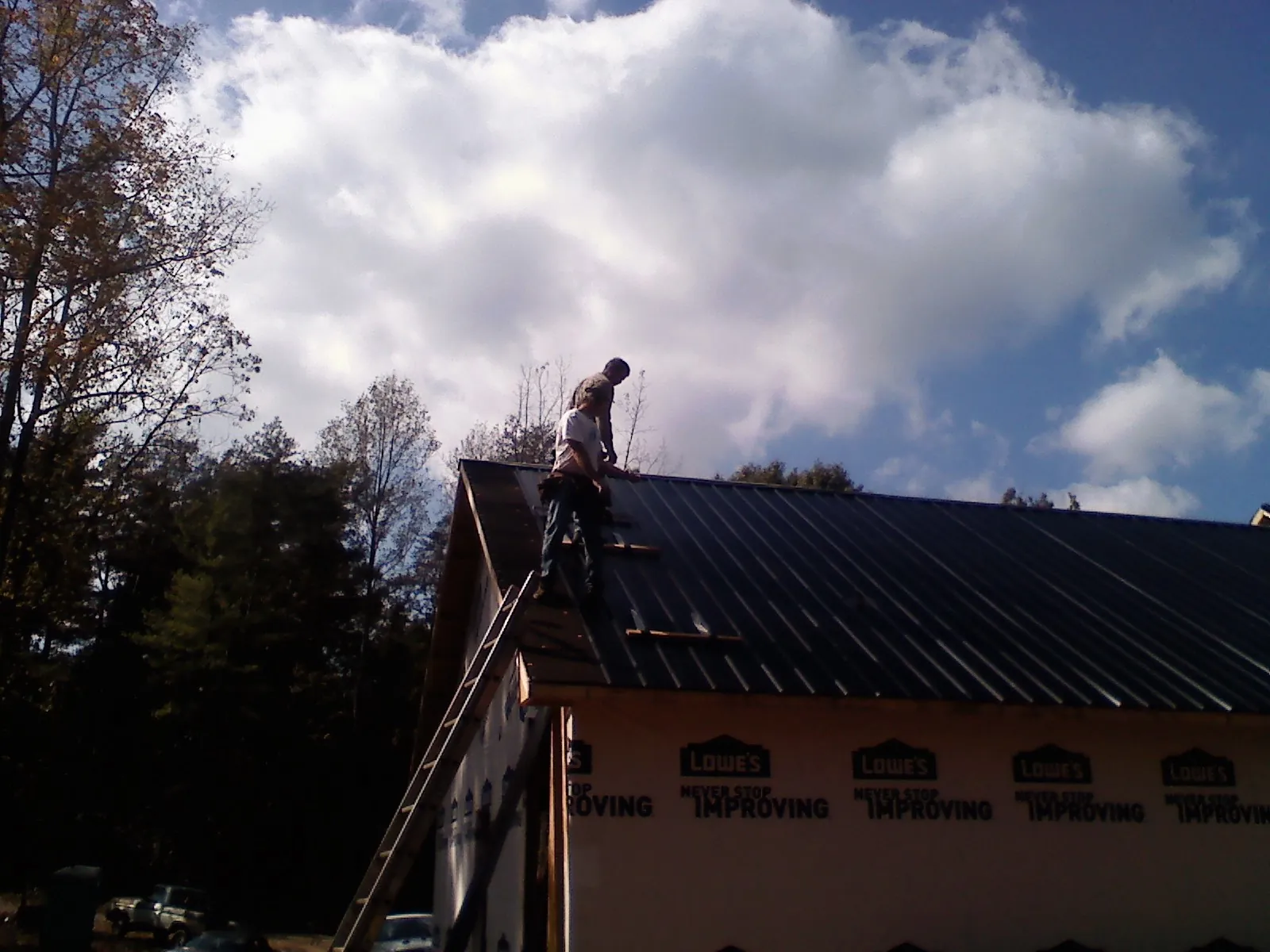 Roofer fastening dark metal panels high against a cloudy sky, from a Roof Inspection job in Hilltown