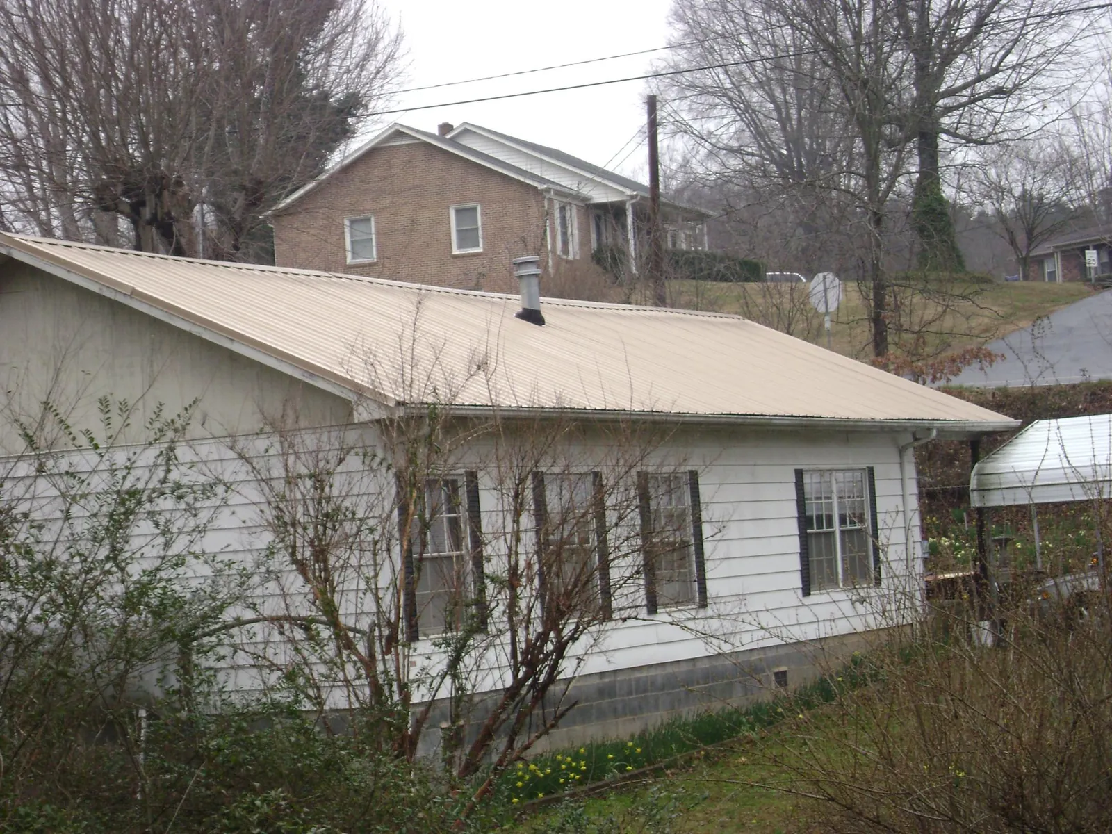 Tan metal roof on a white sided house set into a hillside — Commercial Roofing by Roofing Brothers in Hilltown